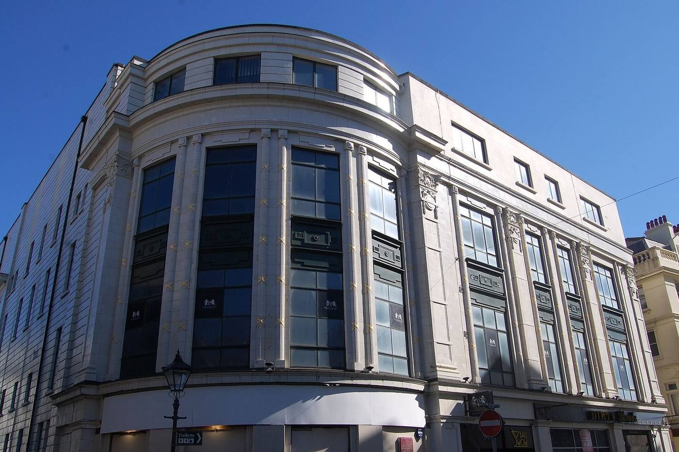 A curved stone-faced commercial building with tall glazed bays and shop units at street level